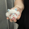 A white cherry blossom plush charm with pink accents is held in a person's hand next to a pearl bracelet.