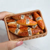A hand holds a woven basket filled with golden croissants and baguettes for a miniature dollhouse set.