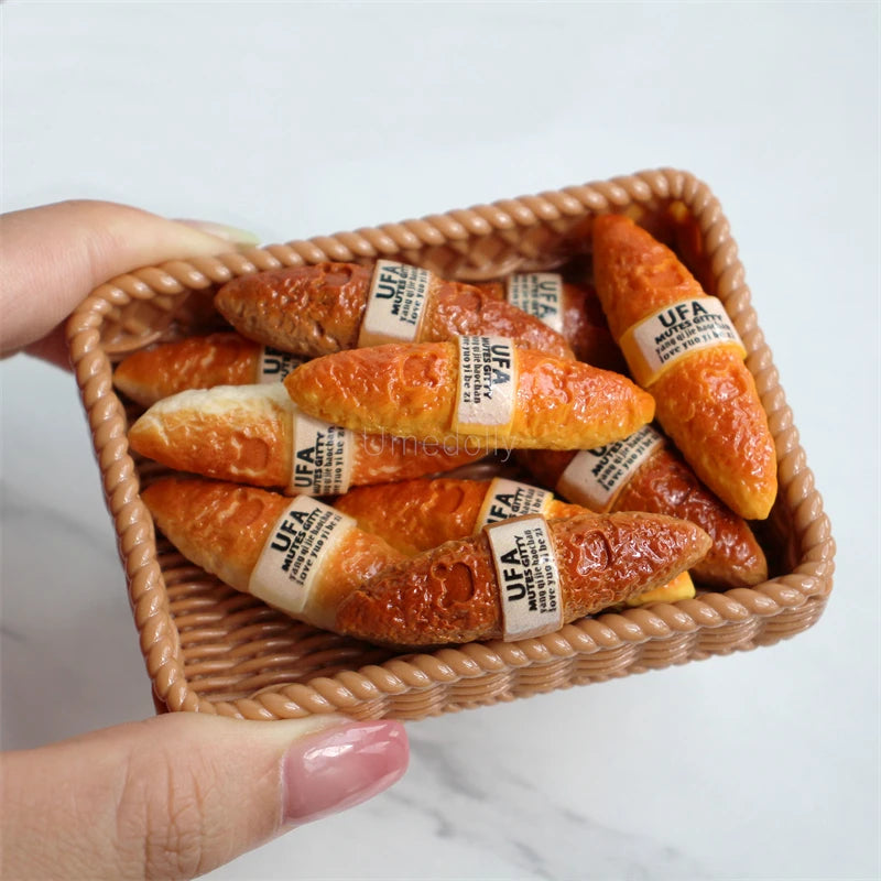 A hand holds a woven basket filled with golden croissants and baguettes for a miniature dollhouse set.