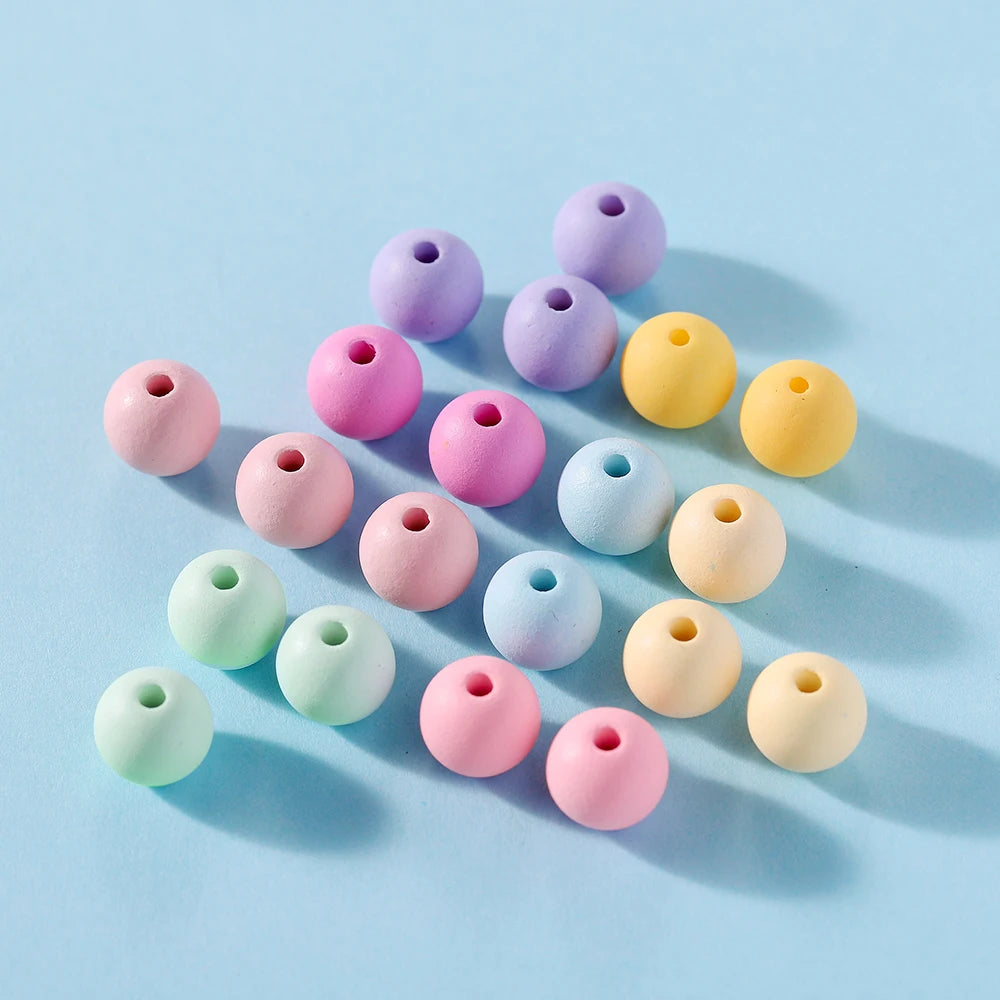A collection of matte acrylic round beads in various pastel colors like purple, pink, yellow, and blue scattered on a light b