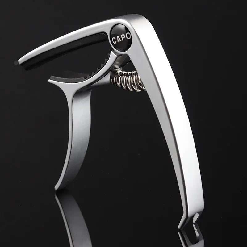 A silver aluminum alloy quick-change guitar capo is shown in a profile view against a dark background.