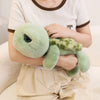 A person is holding a soft green sea turtle plush toy with mottled green and yellow skin against a white shirt.