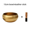A golden copper singing bowl and a leather stick are shown together.