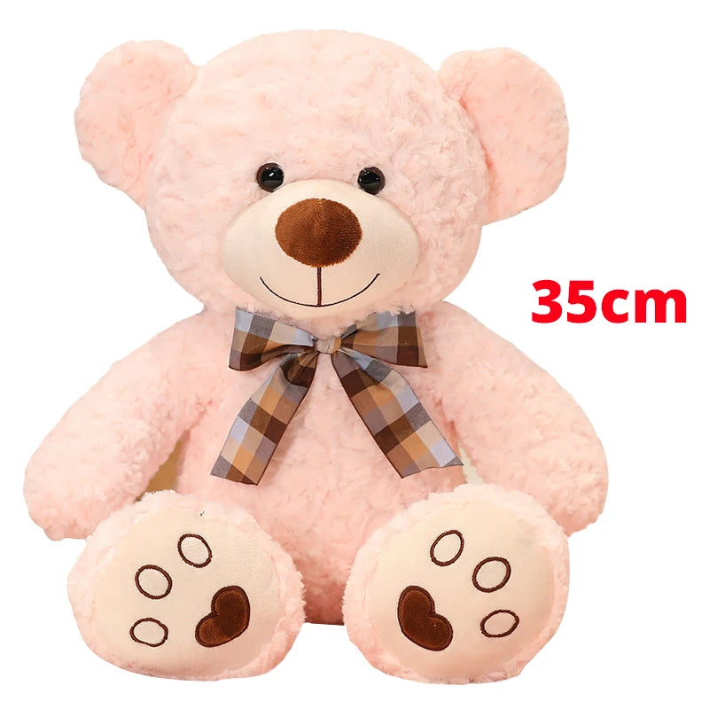 A pink teddy bear plush pillow with a brown nose and a plaid bow.