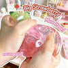 A hand is squeezing a large, translucent pink strawberry squishy stress ball with a green cap.
