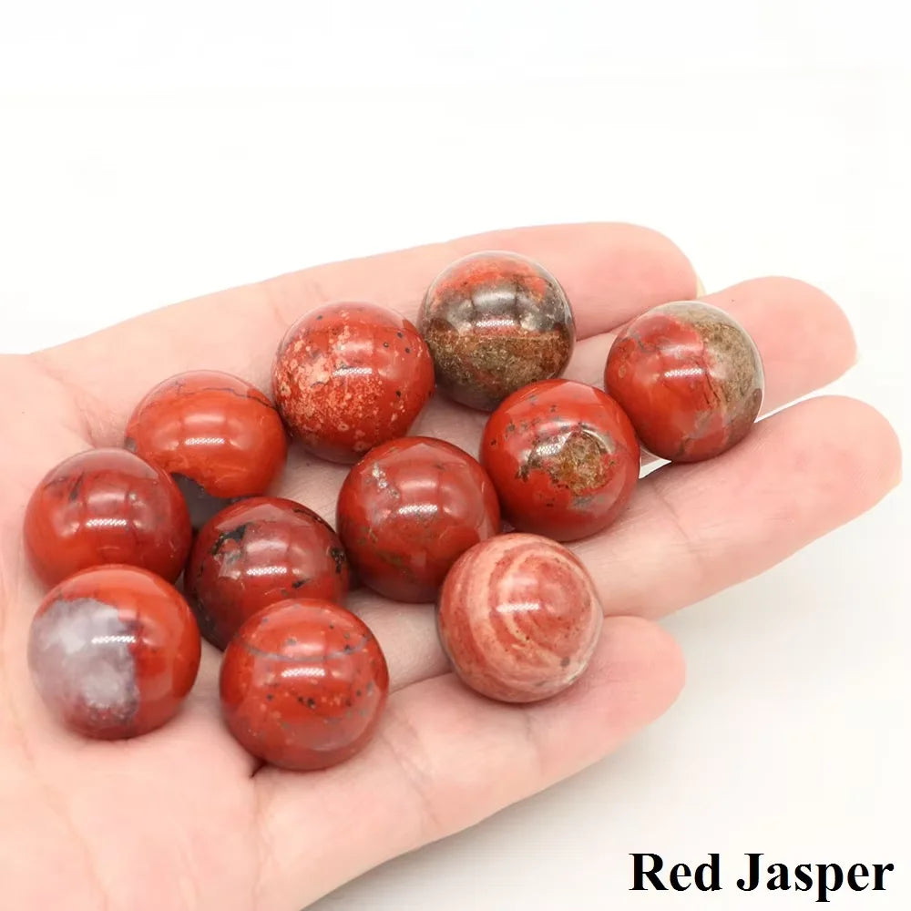 A hand holds several polished red jasper crystal spheres of varying shades and textures.