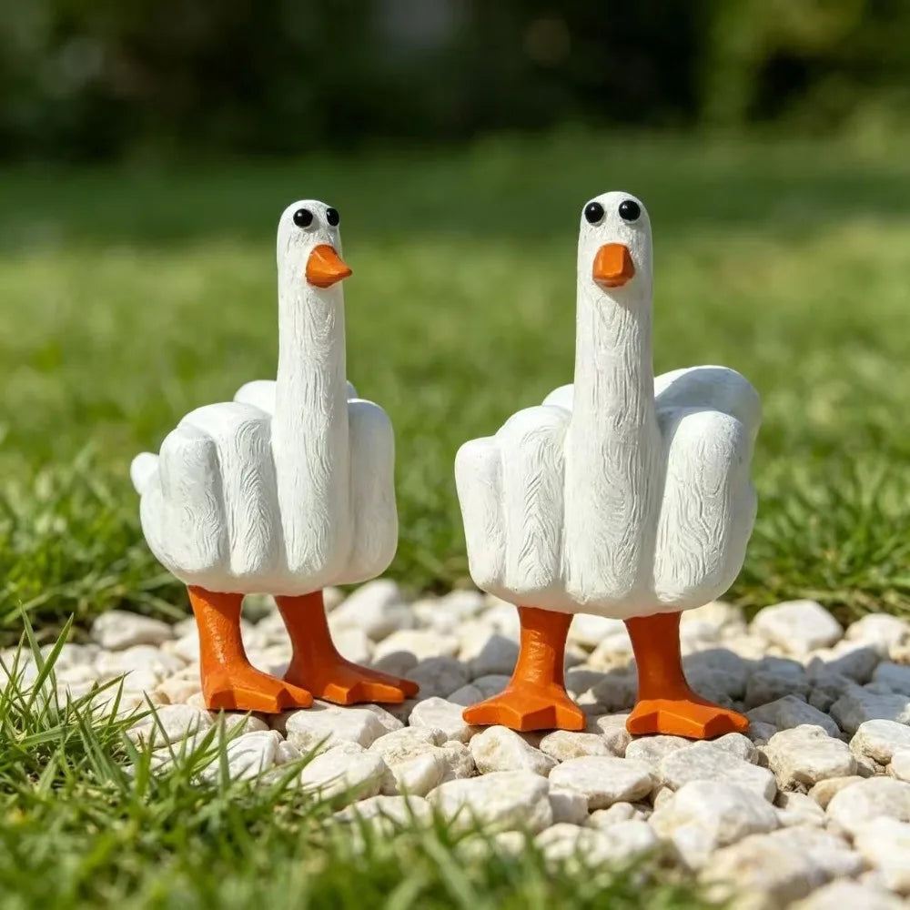 A white resin figurine of a goose with a funny middle finger gesture standing on light gravel.