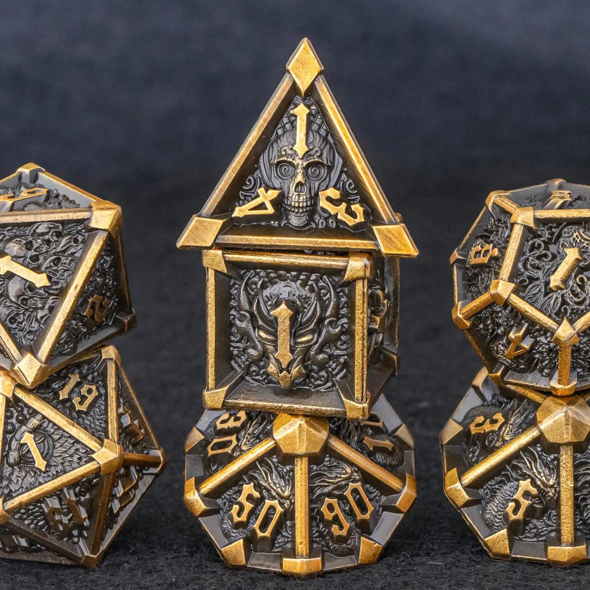 A set of seven metal dice featuring skulls and dragons in gold and dark metal tones.