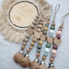 A set of personalized wooden baby pacifier clips featuring silicone beads and a natural fiber wreath.