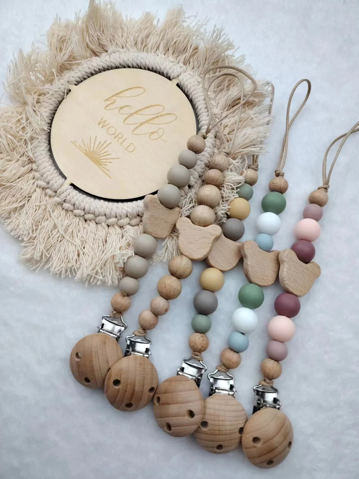 A set of personalized wooden baby pacifier clips featuring silicone beads and a natural fiber wreath.