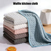 A stack of light-colored and gray waffle kitchen cloths, including a blue-green cloth, next to an orange slice.