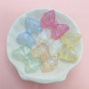 A collection of shimmering pink, blue, and yellow mermaid bowknot beads for jewelry making displayed on a white dish.