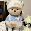 A white teddy bear plush wearing a light blue and white patterned outfit and overalls.