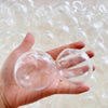 A hand holds a clear, translucent squishy stress ball cover with a refillable shell against a background of similar items.