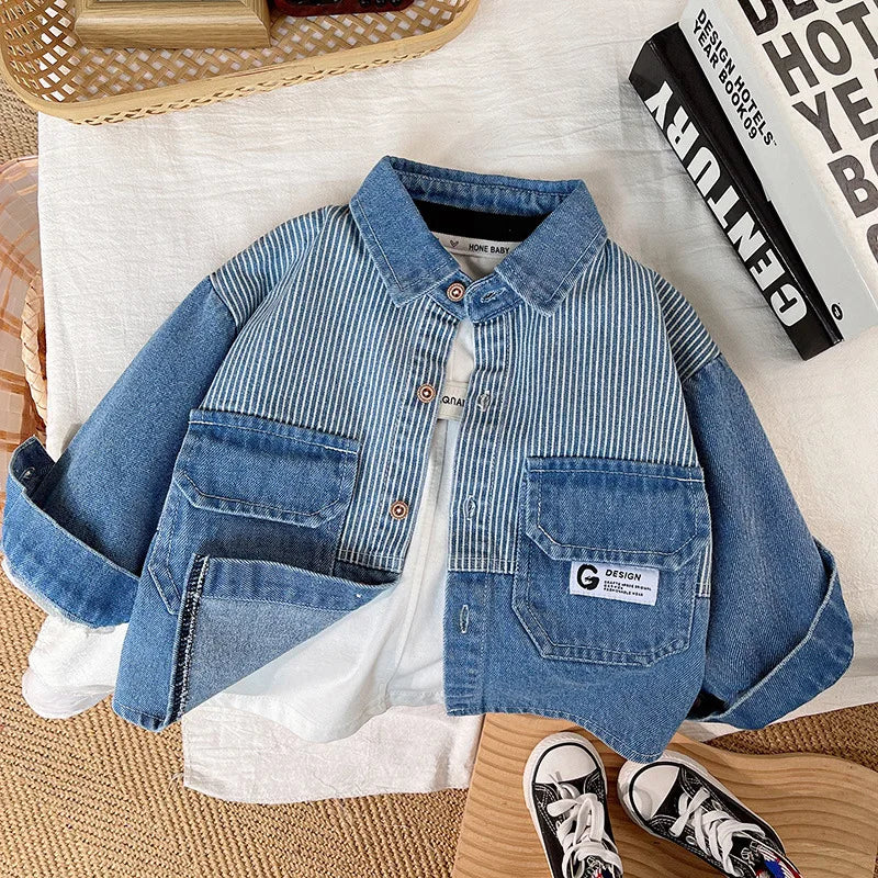 A blue and white striped denim jacket with chest pockets lying on a white fabric background.