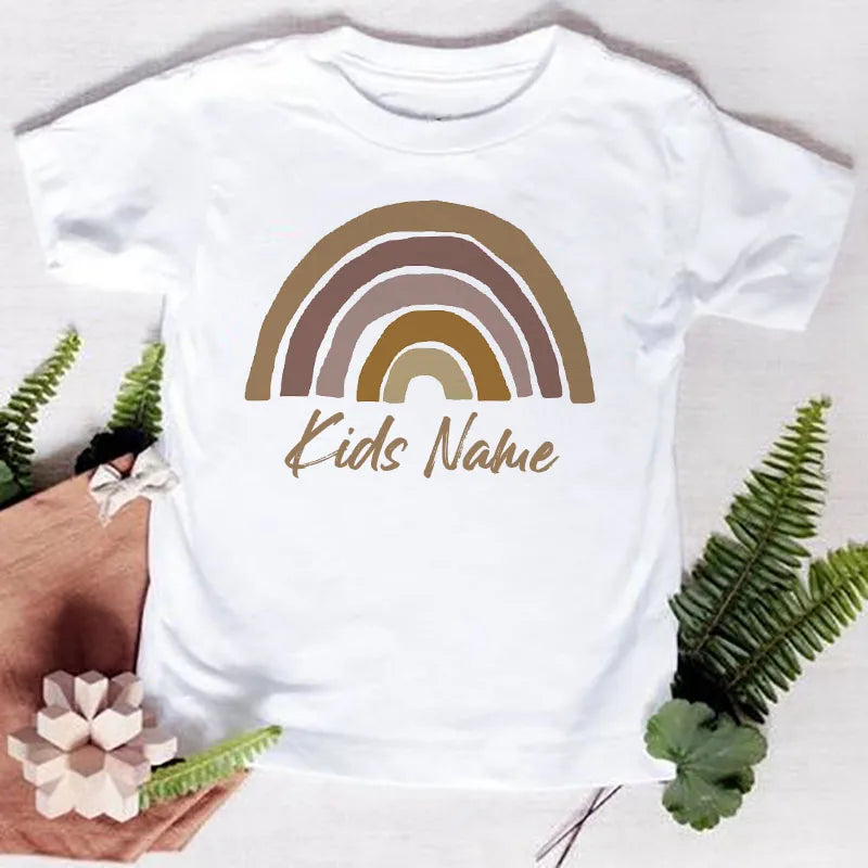 White t-shirt featuring a rainbow graphic and the text Kids Name printed in brown ink.