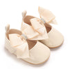 A pair of light beige lace-trimmed baby girl moccasin shoes with fabric bows