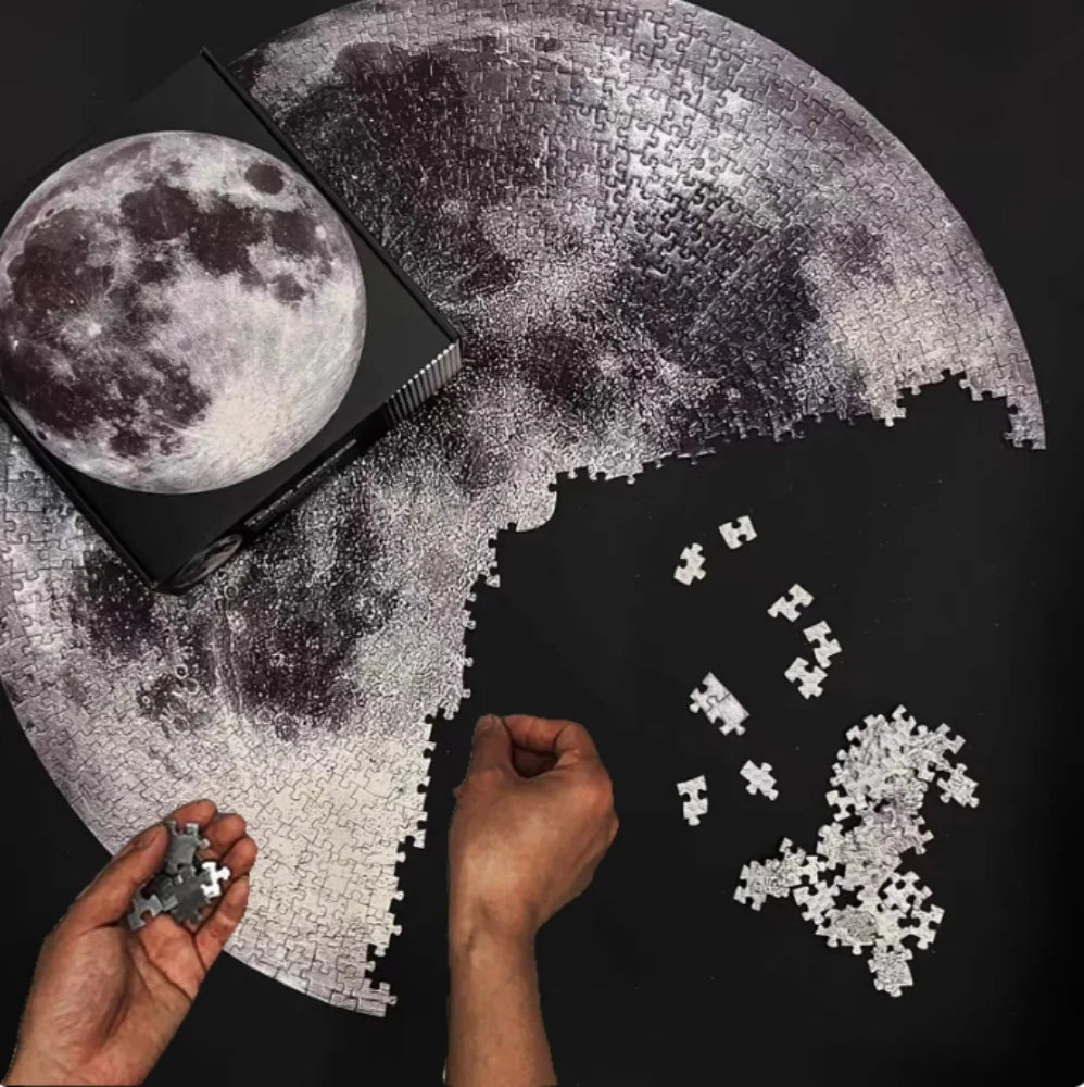 A hand is assembling a jigsaw puzzle of the moon onto a large, curved piece.