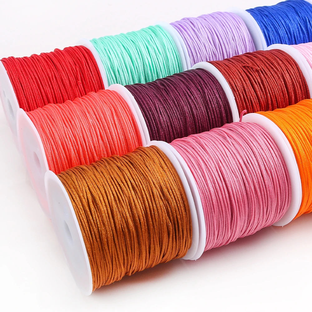 A collection of colorful macrame cord rolls in various shades of red, pink, orange, and blue for jewelry making and crafts.