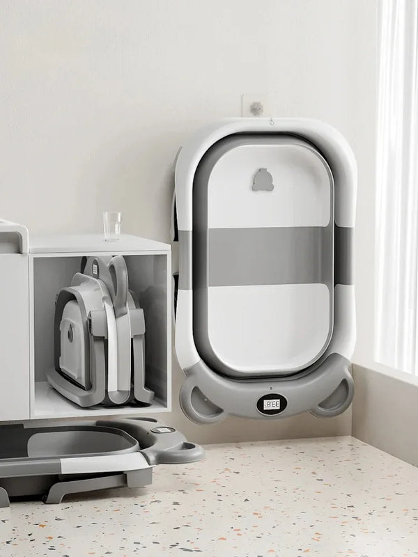 A white collapsible baby bathtub with a gray and white striped design and temperature sensor is shown on a floor.