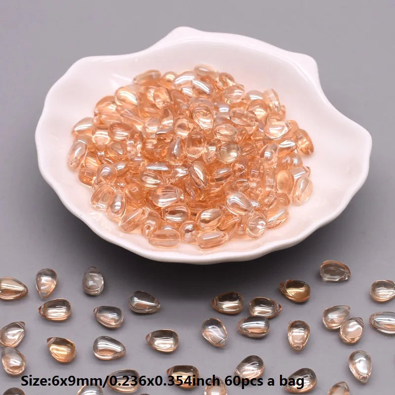 A pile of clear amber water drop Czech glass beads for jewelry making in a white dish.