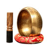 Handmade copper singing bowl with a mallet resting on a red fabric base