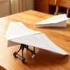 Ein weißes Papierflugzeug-Set mit schwarzem Rahmen und Propeller liegt auf einem Holztable.