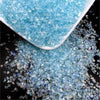 A pile of light blue crushed glass crystals in a white dish and scattered on a dark surface.