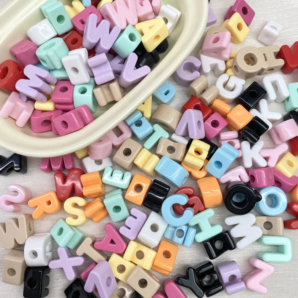 A pile of colorful acrylic letter beads in various shades including pink, purple, yellow, and black.