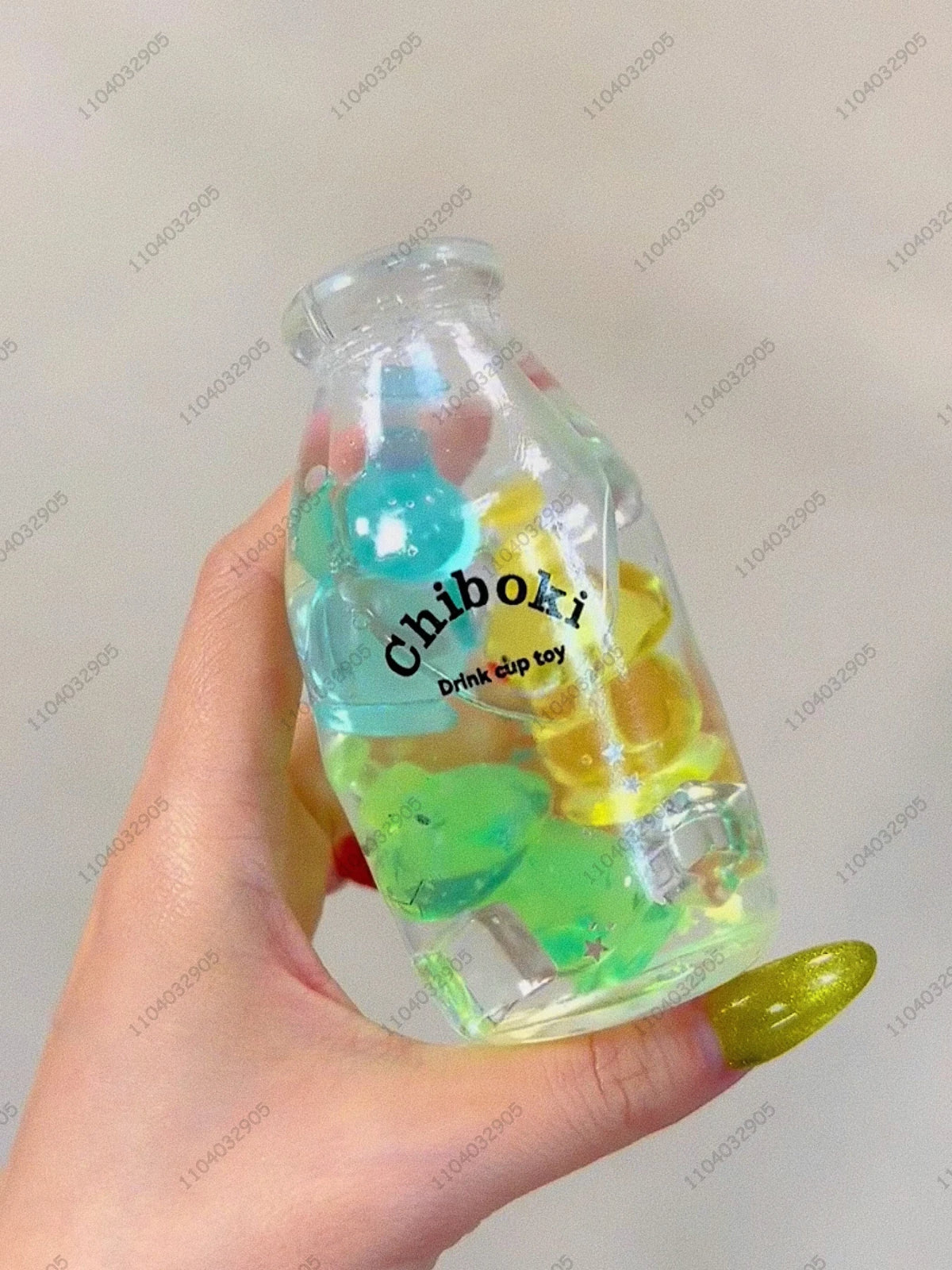 A hand holds a clear plastic bottle filled with colorful squishy toys, labeled Chiboki drink cup toy.