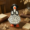 A white goose statue dressed in a black plaid dress and bow, sitting on a wooden surface with books.