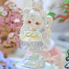 A white collectible figurine of a cute girl with pink hair and large eyes, sitting on a decorative base.