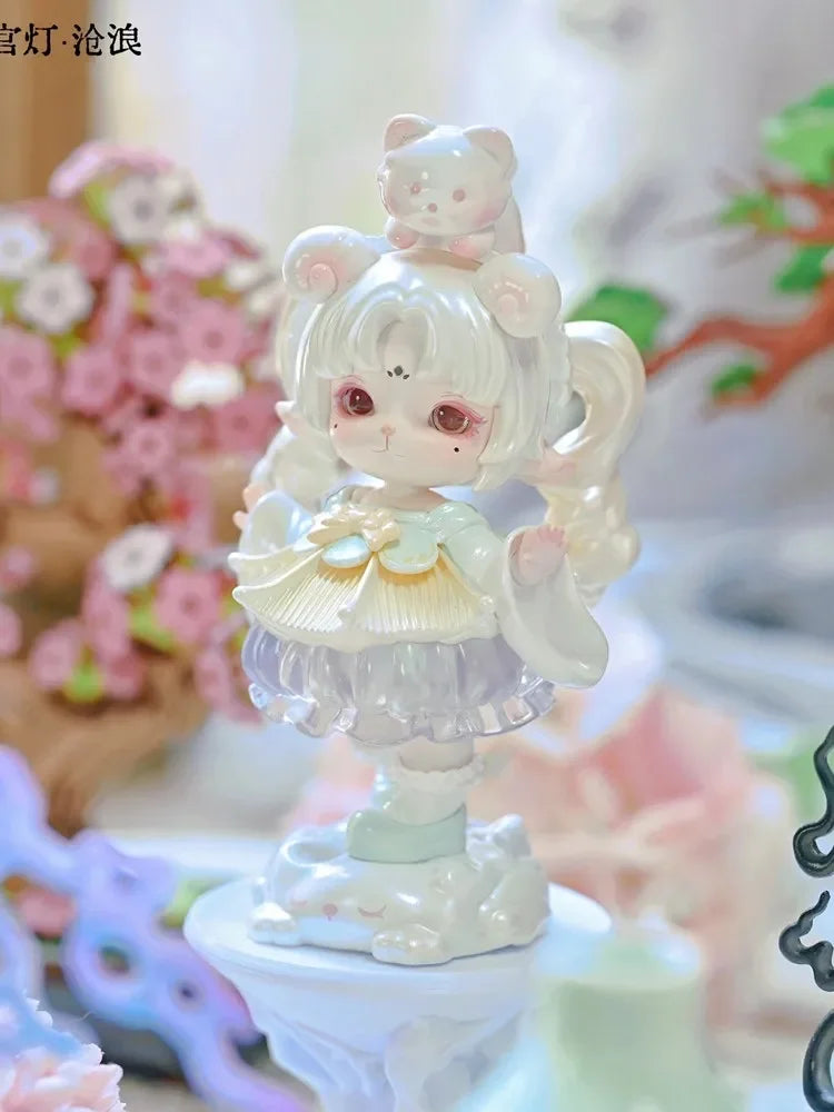 A white collectible figurine of a cute girl with pink hair and large eyes, sitting on a decorative base.