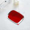 A shiny red emblem car badge decal is placed on a white surface next to a glass bottle and white flowers.