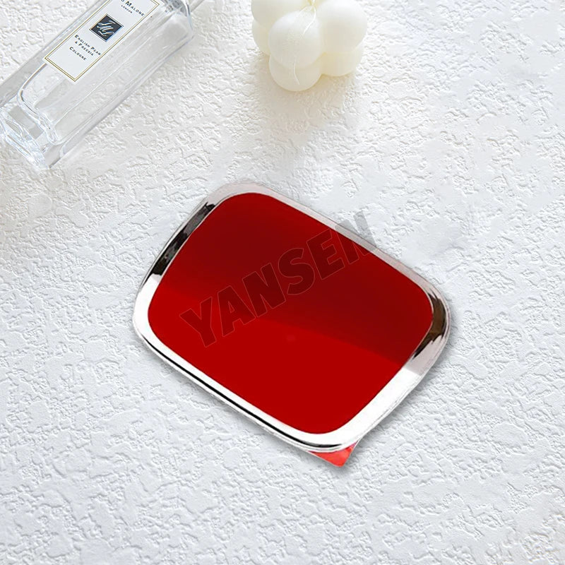 A shiny red emblem car badge decal is placed on a white surface next to a glass bottle and white flowers.