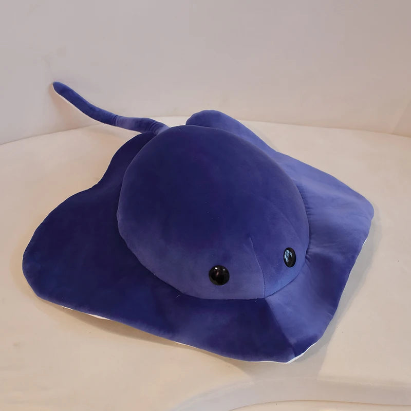 A dark blue plush toy shaped like a devil fish with a long tail and large eyes.