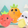 An orange plush toy shaped like a fruit, a red strawberry plush, and a yellow banana plush are displayed against a light blue