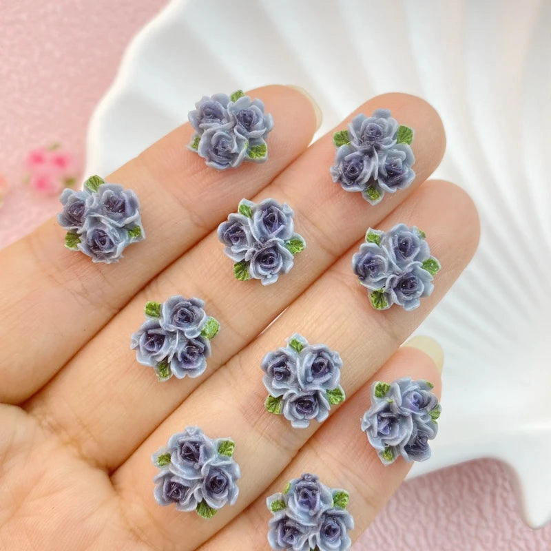 A hand holds a set of three resin flower ornaments in shades of purple and blue.