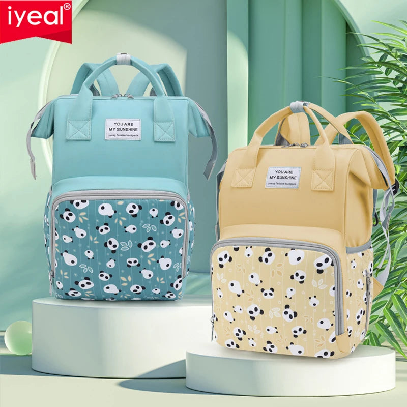 A light blue mommy backpack with a patterned fabric and a yellow mommy backpack displayed on a white stand.