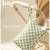A green checkered fabric bag is shown hanging from a wooden handle on a light-colored stroller or carrier.