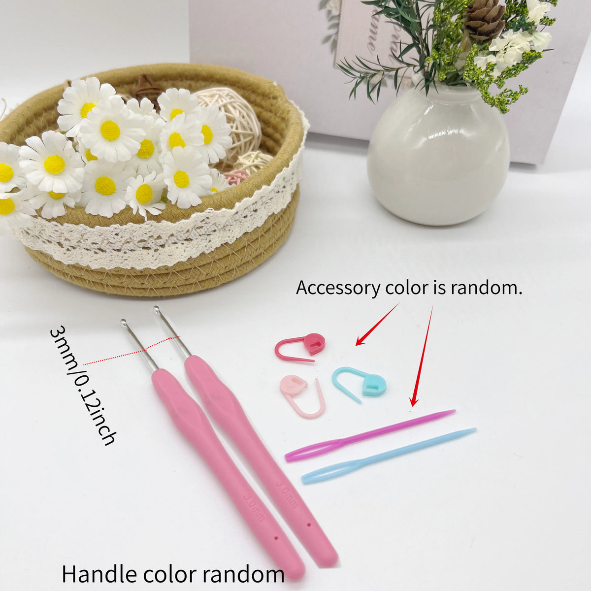 A set of pink crochet hooks, stitch markers, and needles are displayed next to a woven basket and flowers.