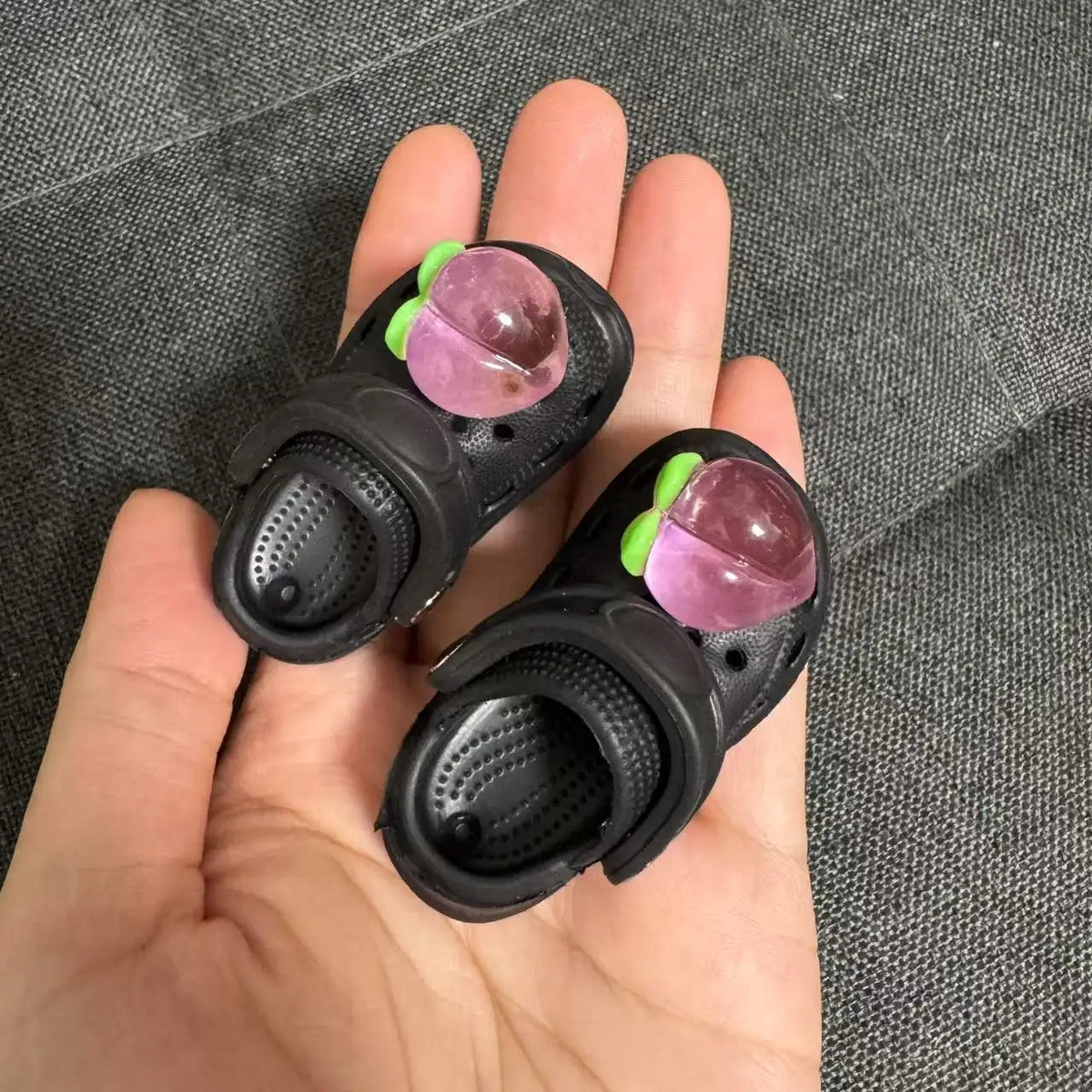 A hand holds a black fashion slipper accessory with pink and green gems for 1/6 BJD dolls.