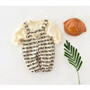 A cream and black striped baby romper with a bear decoration lying next to an orange hat and a green leaf.