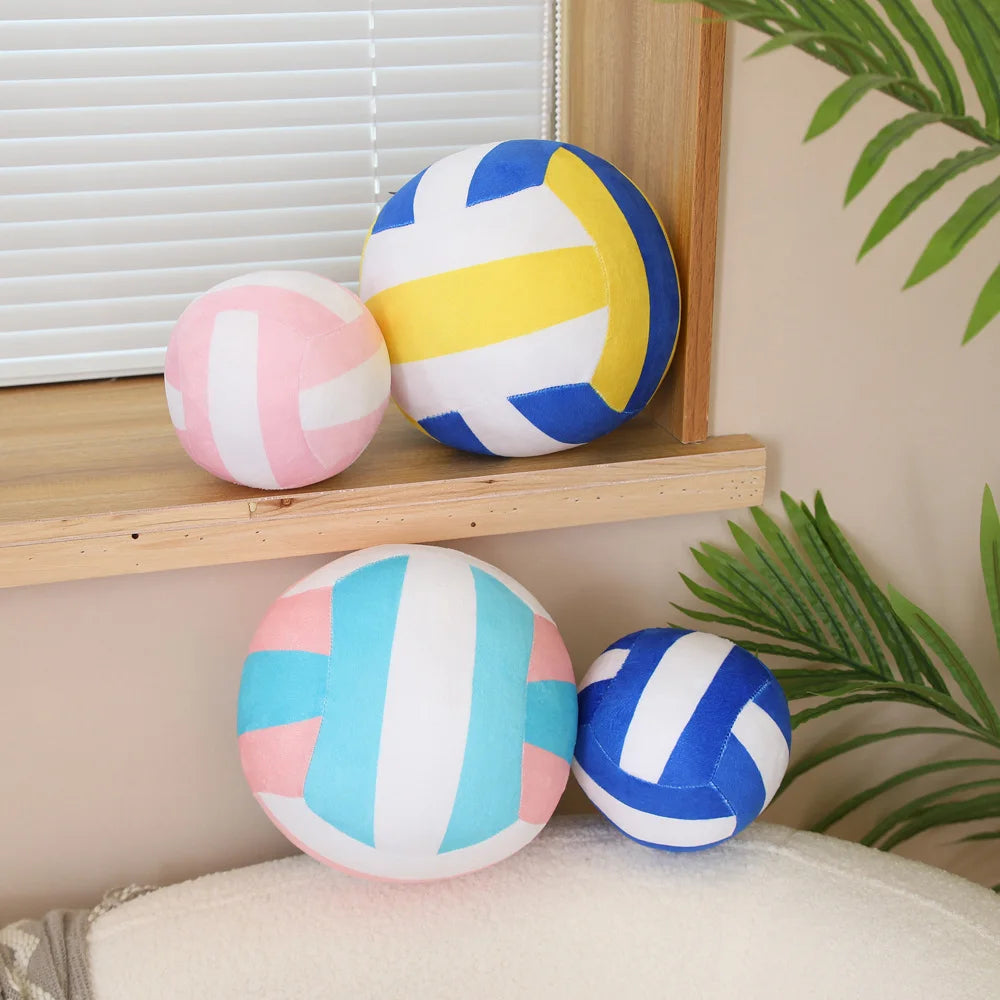 A collection of colorful soft plush volleyball pillows in yellow, pink, and blue resting on a wooden shelf.