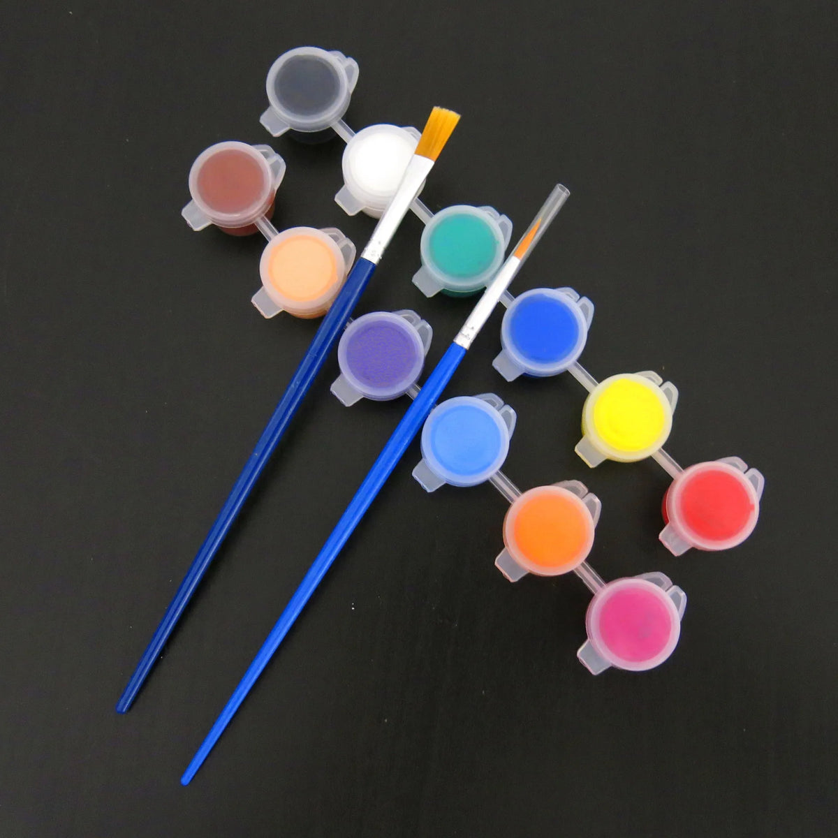 A set of twelve acrylic paint colors in small pots with brushes arranged on a dark surface.