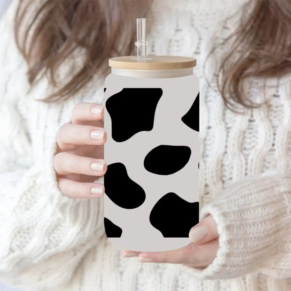 A hand holds a clear cup wrap featuring a black and white leopard print design against a light background.