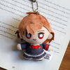 A plushie pendant charm of an anime character with reddish-brown hair and large red eyes resting on a piece of paper.