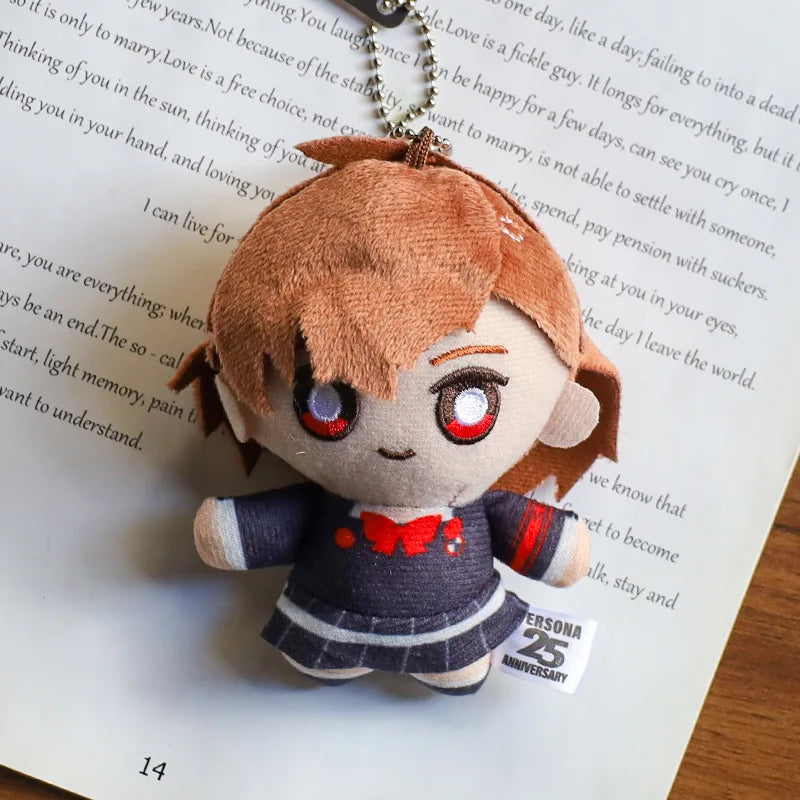 A plushie pendant charm of an anime character with reddish-brown hair and large red eyes resting on a piece of paper.