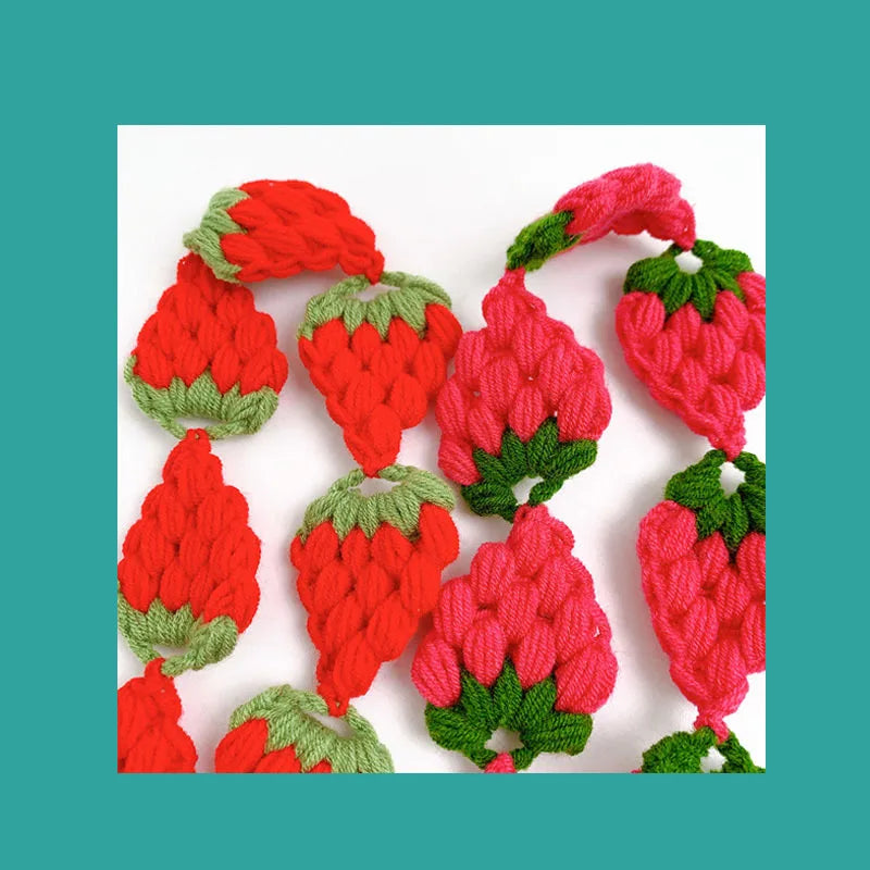 A close-up of a red strawberry crochet headband with green leaves and a wide elastic band.
