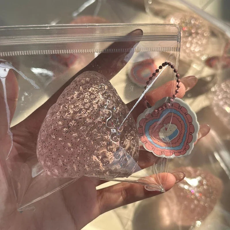 A hand holds a pink strawberry squishy fidget toy inside clear packaging.